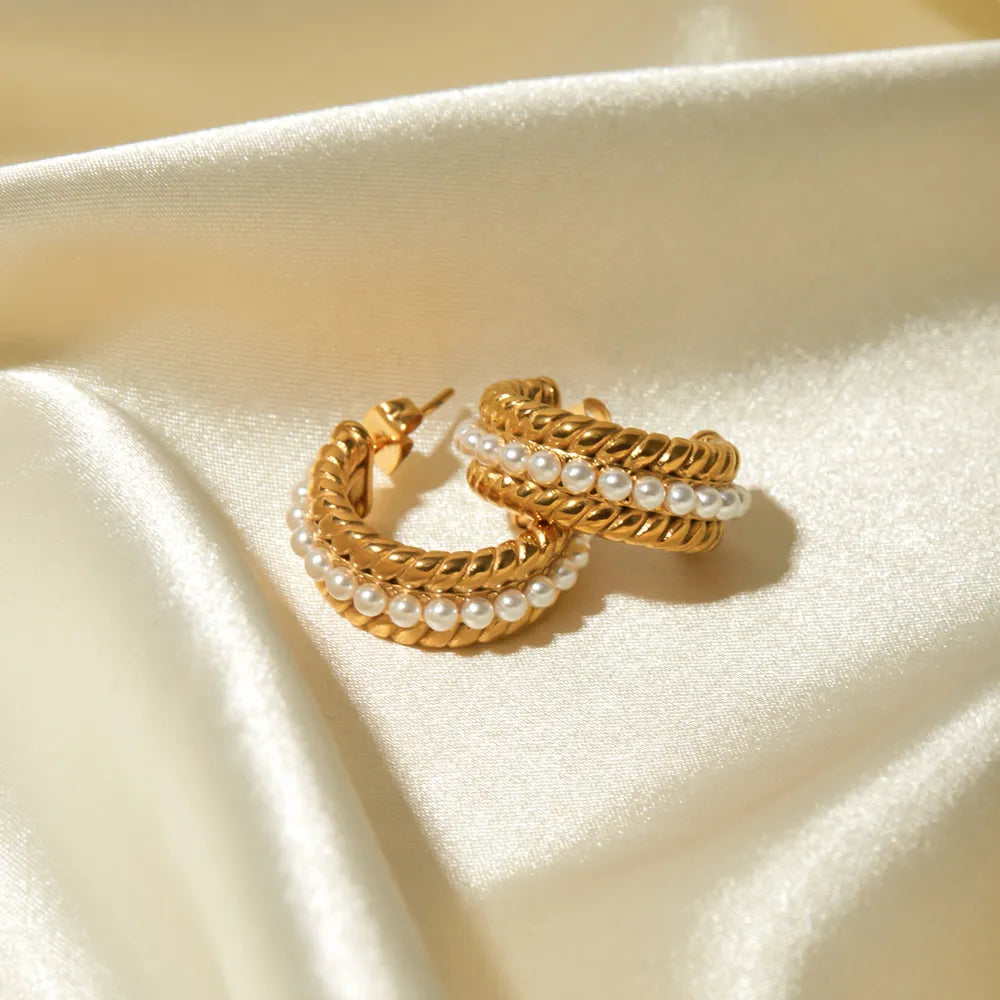 Gold stainless steel pearl C-hoop earrings, 18K gold-plated, displayed on satin fabric background for luxury presentation.