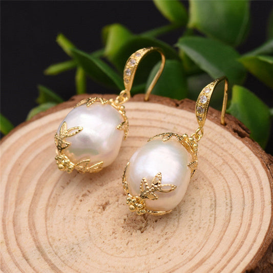 Pearl earrings with gold accents on a wooden surface with green leaves in the background