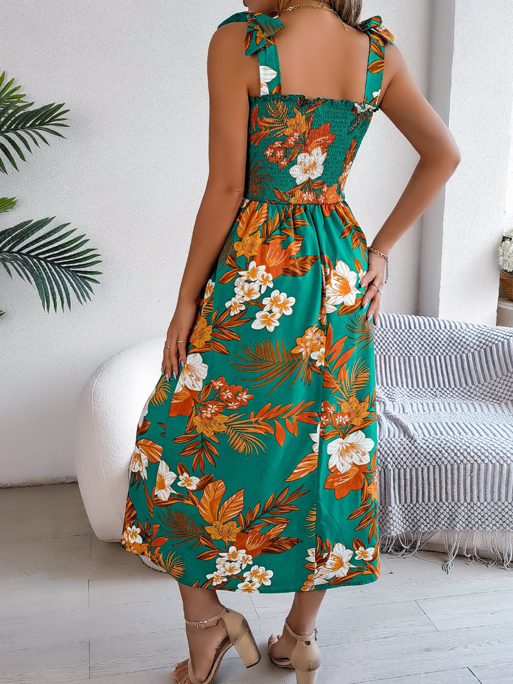 Woman wearing a floral dress in a room with a white wall and a plant.