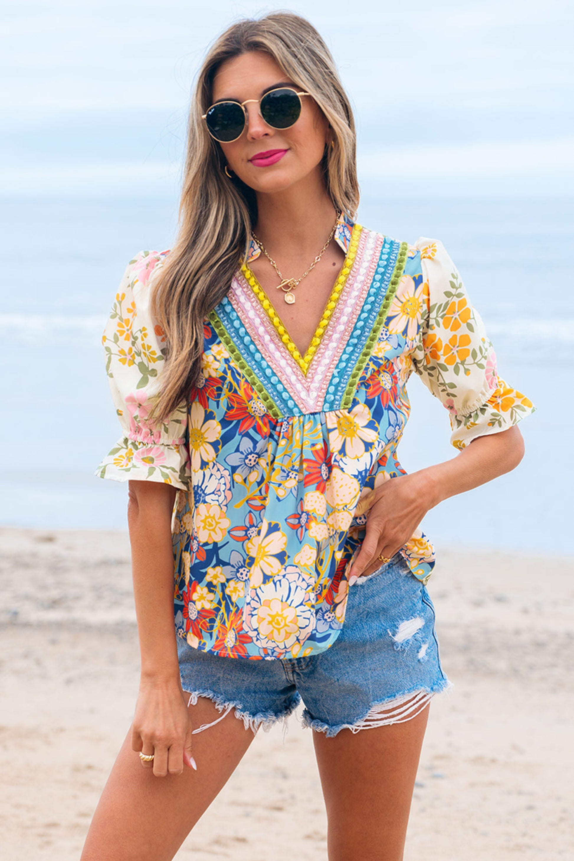 Woman in a colorful floral top and denim shorts on a beach.