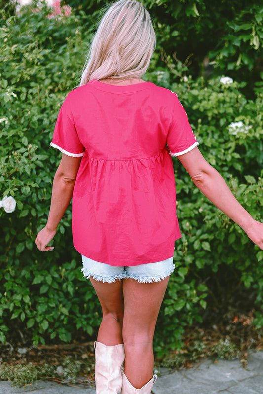 Person wearing a pink top and white shorts with pink boots, standing in front of green bushes.
