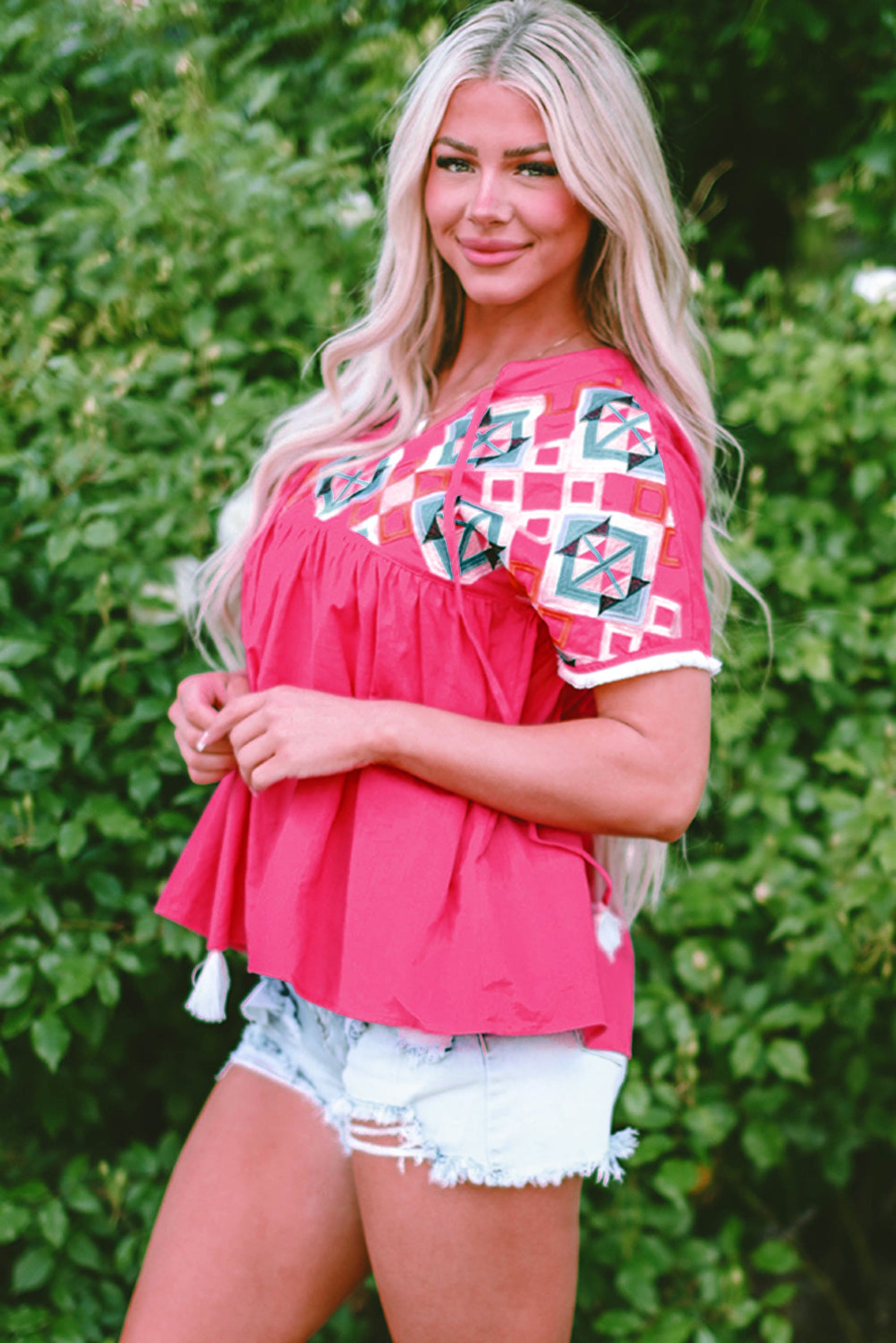 Woman wearing a pink top with geometric patterns against a green leafy background