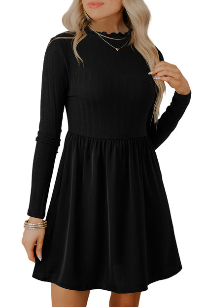 Woman wearing a black long-sleeve skater dress with a fitted top and flared skirt, accessorized with layered necklaces, standing against a light neutral backgroun