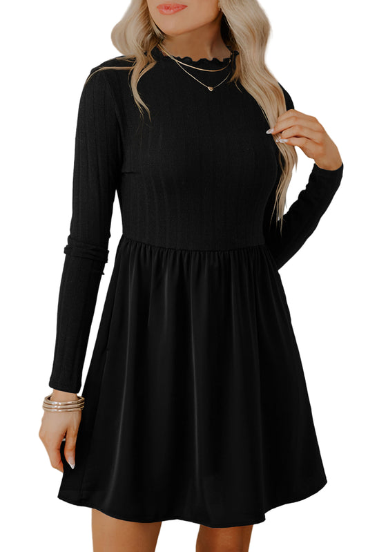 Woman wearing a black long-sleeve skater dress with a fitted top and flared skirt, accessorized with layered necklaces, standing against a light neutral backgroun