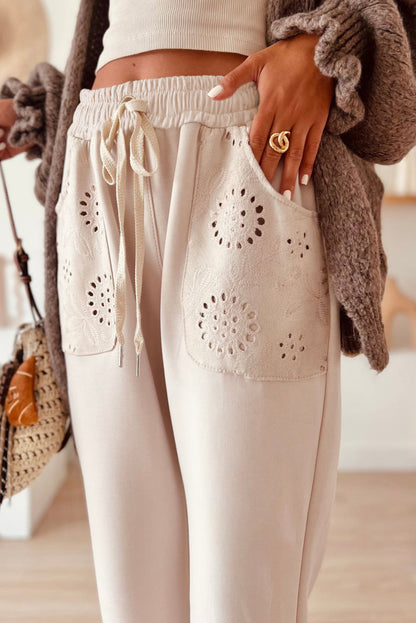 Beige pants with lace detailing worn by a person, with a blurred background.