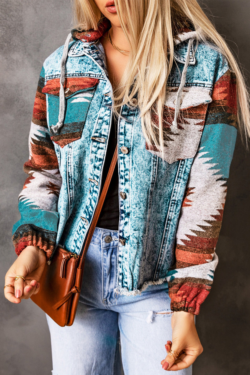 Women’s multicolor Aztec denim jacket with hood and frayed hem, styled with jeans and leather handbag”