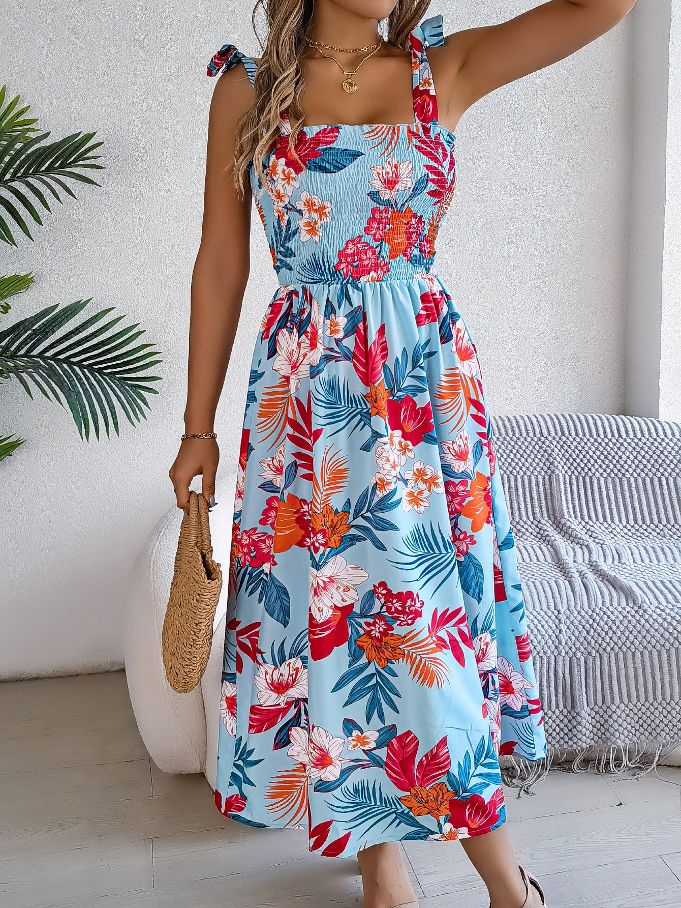 Woman wearing a colorful floral dress in a room with a plant and chair.