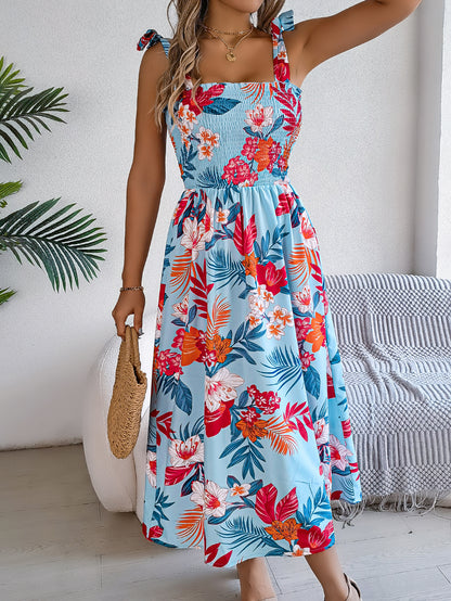 Woman wearing a colorful floral dress in a room with a plant and chair.
